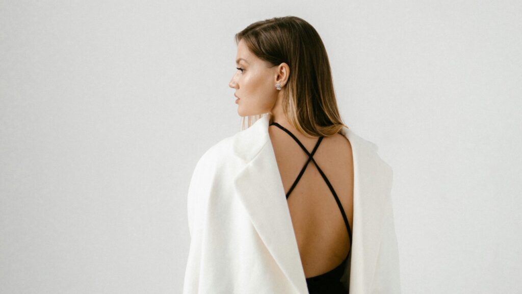 Mujer con blazer blanca de espalda abierta, look elegante en tonos claros y estética minimalista.