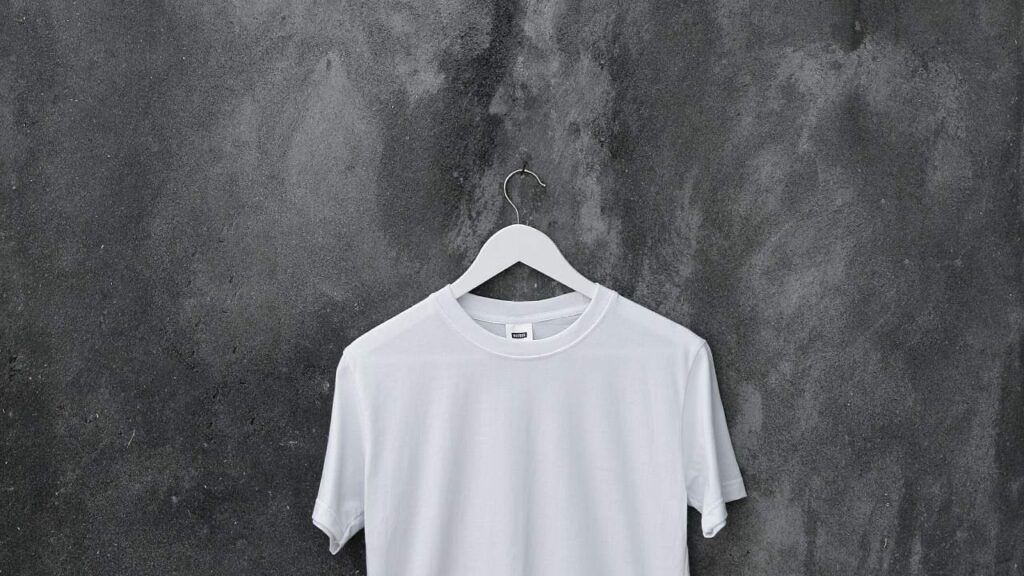 Camiseta blanca colgada sobre una pared gris, símbolo de básico versátil para armario cápsula.