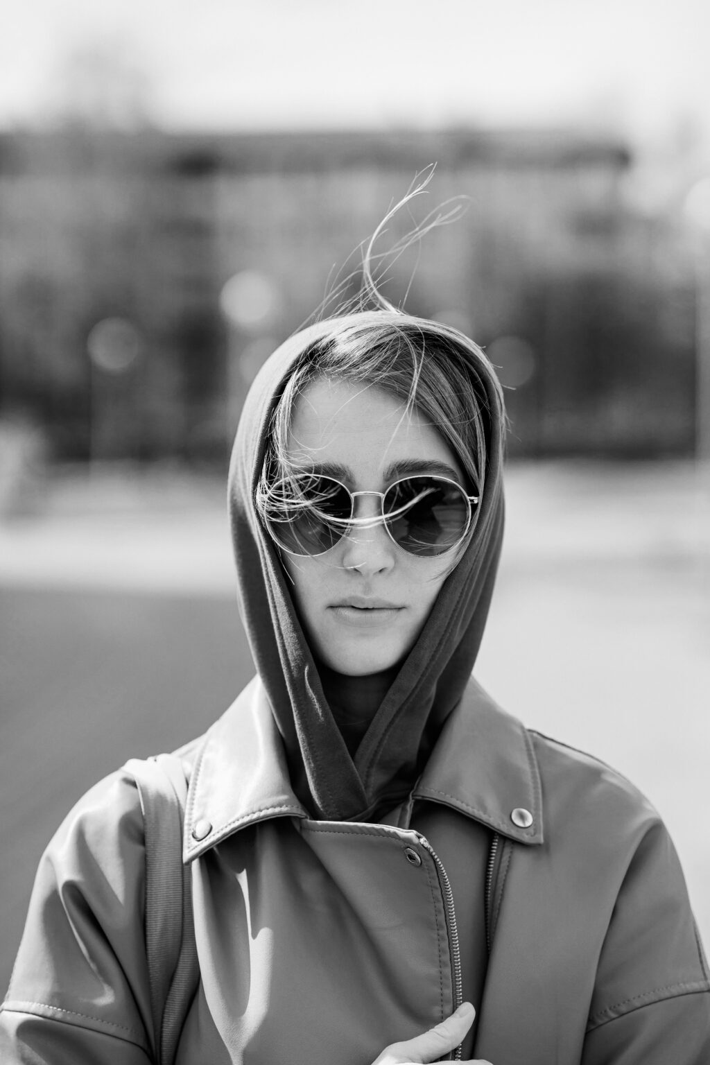 Retrato en blanco y negro de mujer con gafas de sol y capucha, estética urbana y moderna.